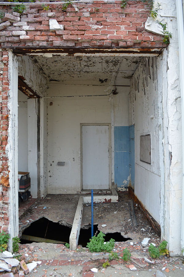 Exterior wall exposed deteriorated brick due to spalled stucco exterior. Floor is deteriorated and has fallen in. 