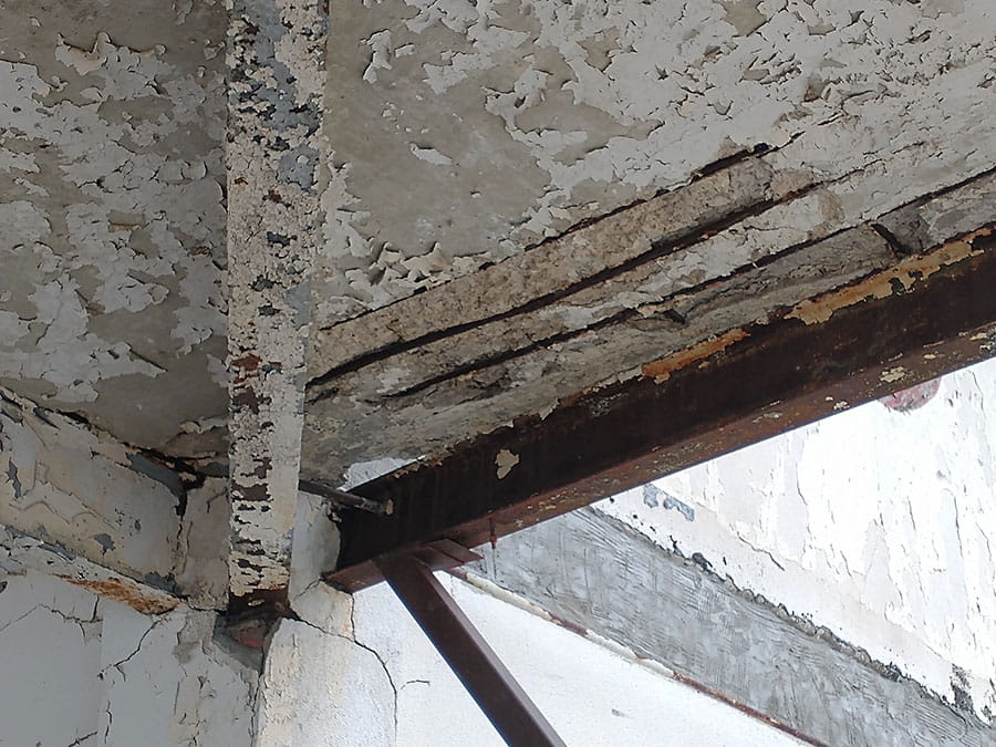 Exterior concrete ceiling with metal beam rusting and paint chipping off.