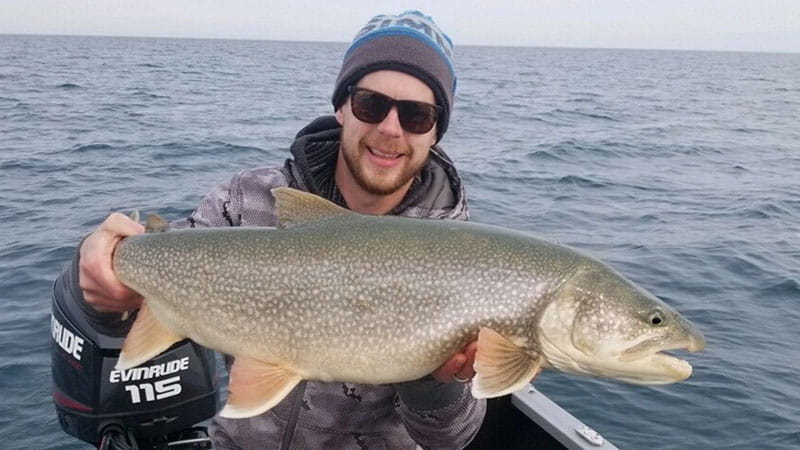 A large lake trout being held up by a person in a boat on the lake