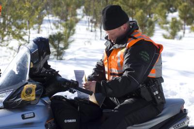an officer sits on a snowmobile writing on a pad