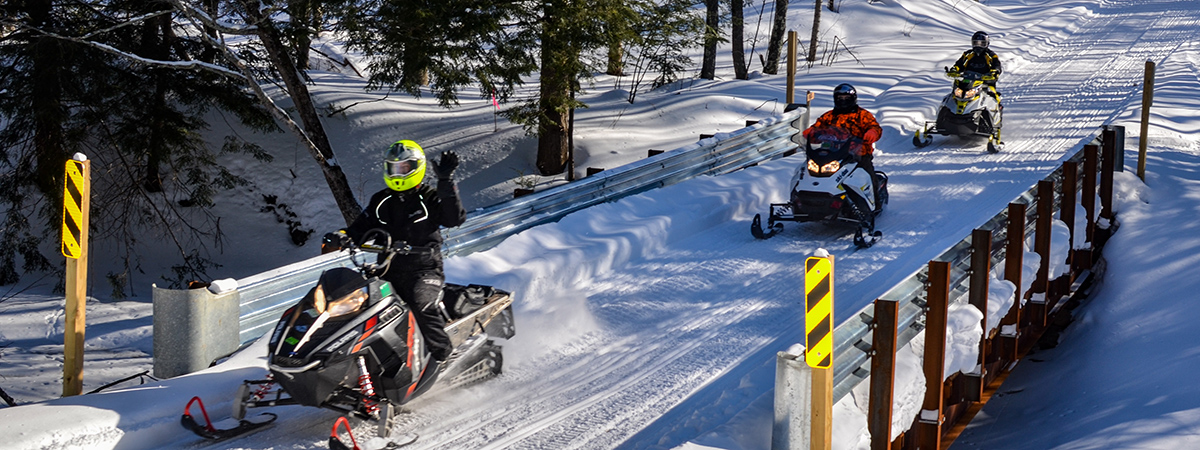 Snowmobilers riding over a trail bridge