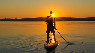 A person on a stand-up paddleboard on a calm lake, silhouetted by a sunset
