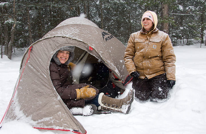two campers posed in front of a tent in snowy conditions
