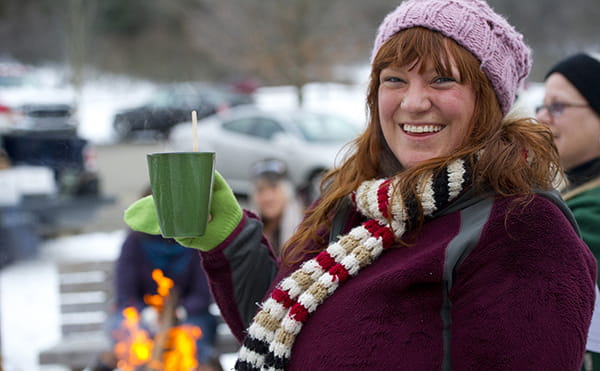smiling visitor holding mug at campfire