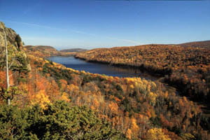 A long lake sits between two tall, forested hills in autumn.