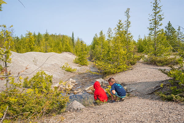 kids kneeling by stream surrounded by rocks