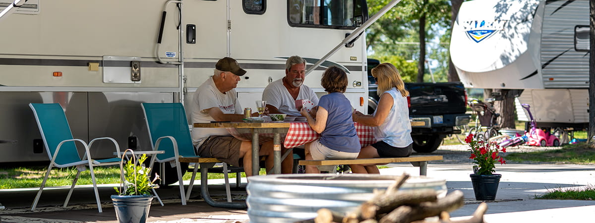 Two couples sitting at picnic table in front of an RV