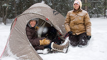 two woman sitting with tent in snow