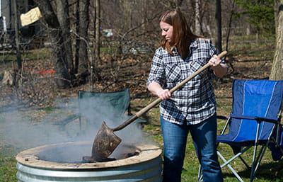 A woman stirring ashes to ensure the fire is out.