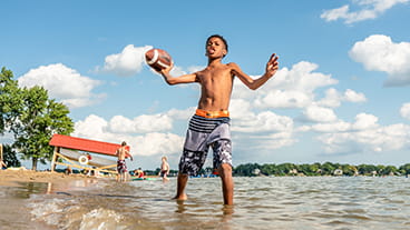 A child throws a football while standing in the water a the beach at Dodge No 4 State Park