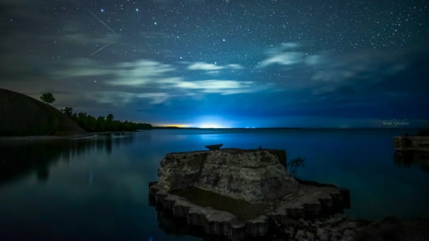 A lake scene at night with the starry skies reflecting in the water below