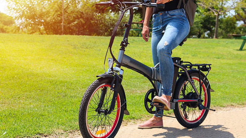 A person on an e-bike on a paved path on a sunny day with green grass in the background