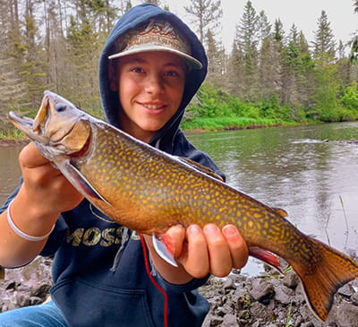 A child holds up a brook trout with a river in the background