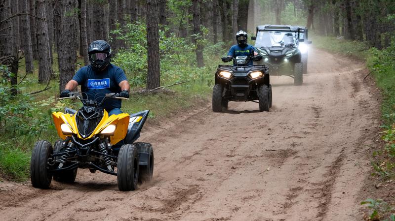 ORV riders on a trail in the woods showing several different ORV types