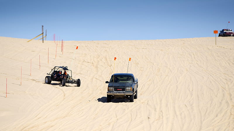two trucks and a buggy riding on the sand dune