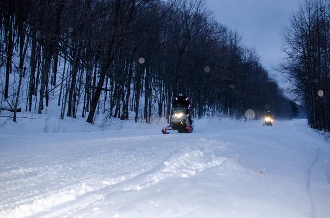 Snowmobilers ride on a trail at Porcupine Mountains Wilderness State Park at dusk with their lights on