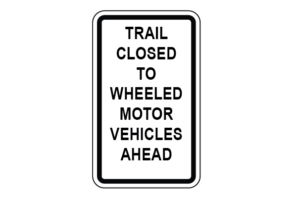 White sign with black text that reads "Trail closed to wheeled motor vehicles ahead"