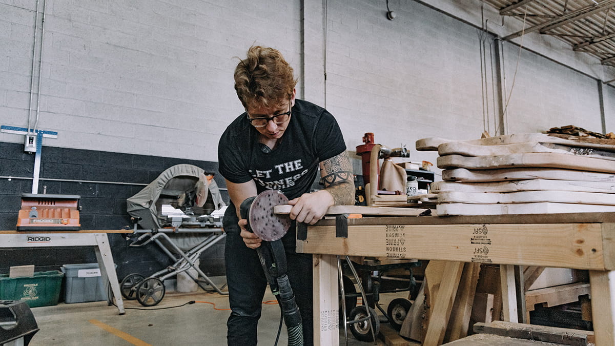 A woodworker leans over a table covered in equipment