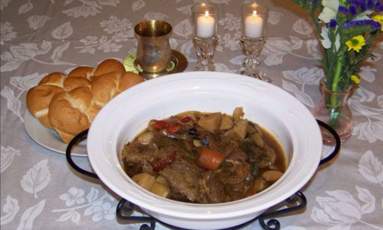 A bowl of stew with some bread by candlelight. 
