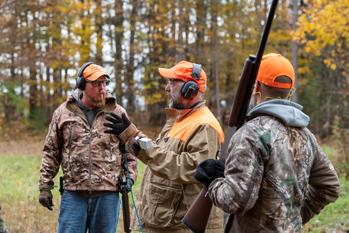 Two hunters receiving instructions on hunting in a forest clearing. 