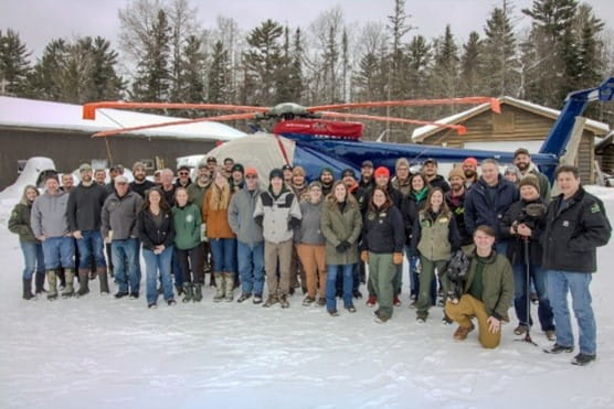 The moose research team poses in front of a helicopter. 