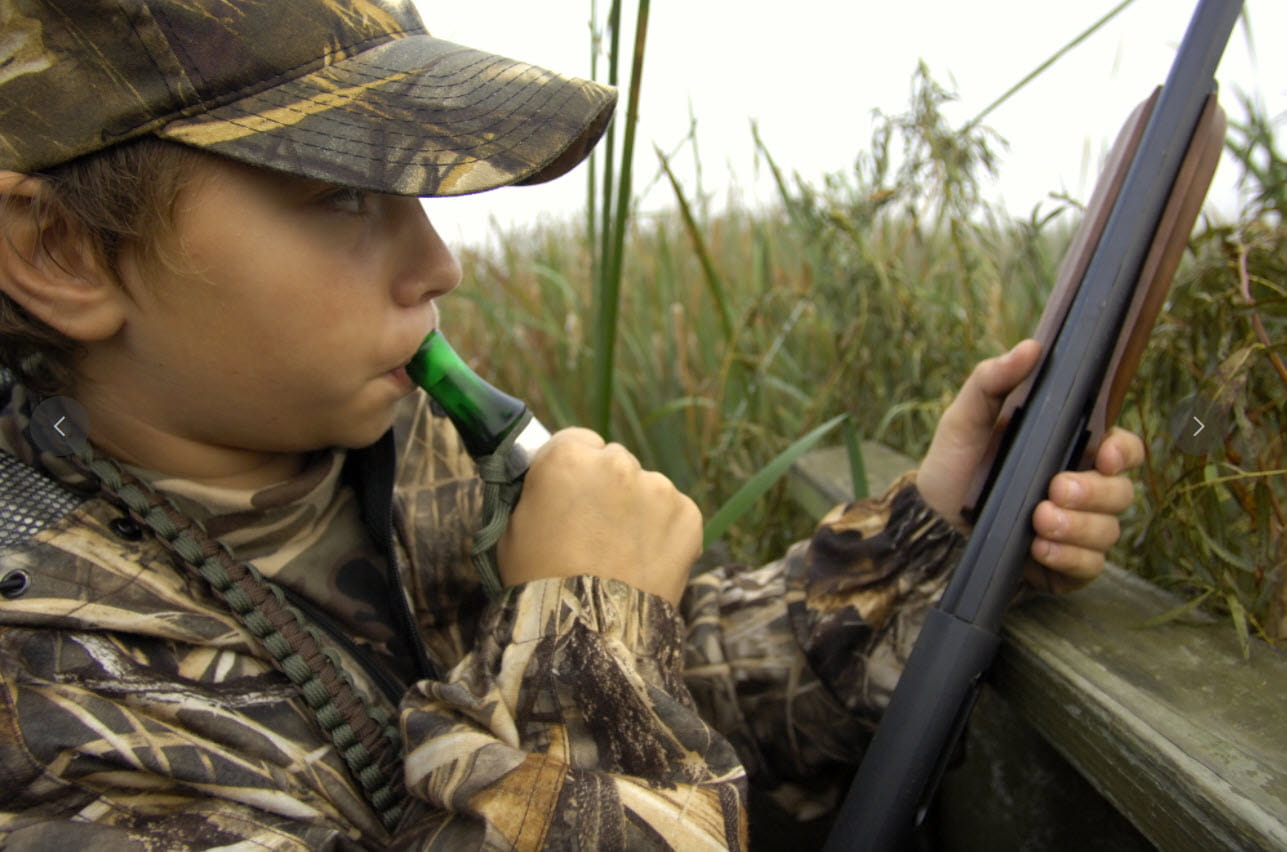 A youth waterfowl hunter using a duck call in a swampy area. 