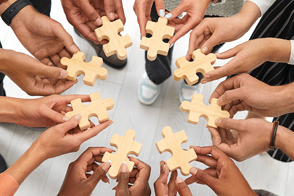 A circle of hands holding puzzle pieces. 