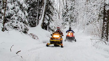 Two snowmobiles riding on a snowmobile trail