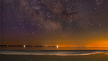 A winter nighttime scene of a starry sky over frozen lake