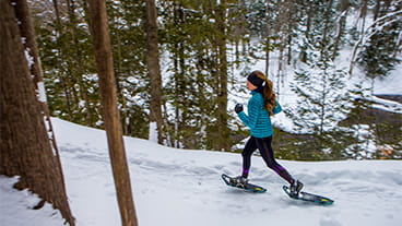 a snowshoer running along tree-lined trail