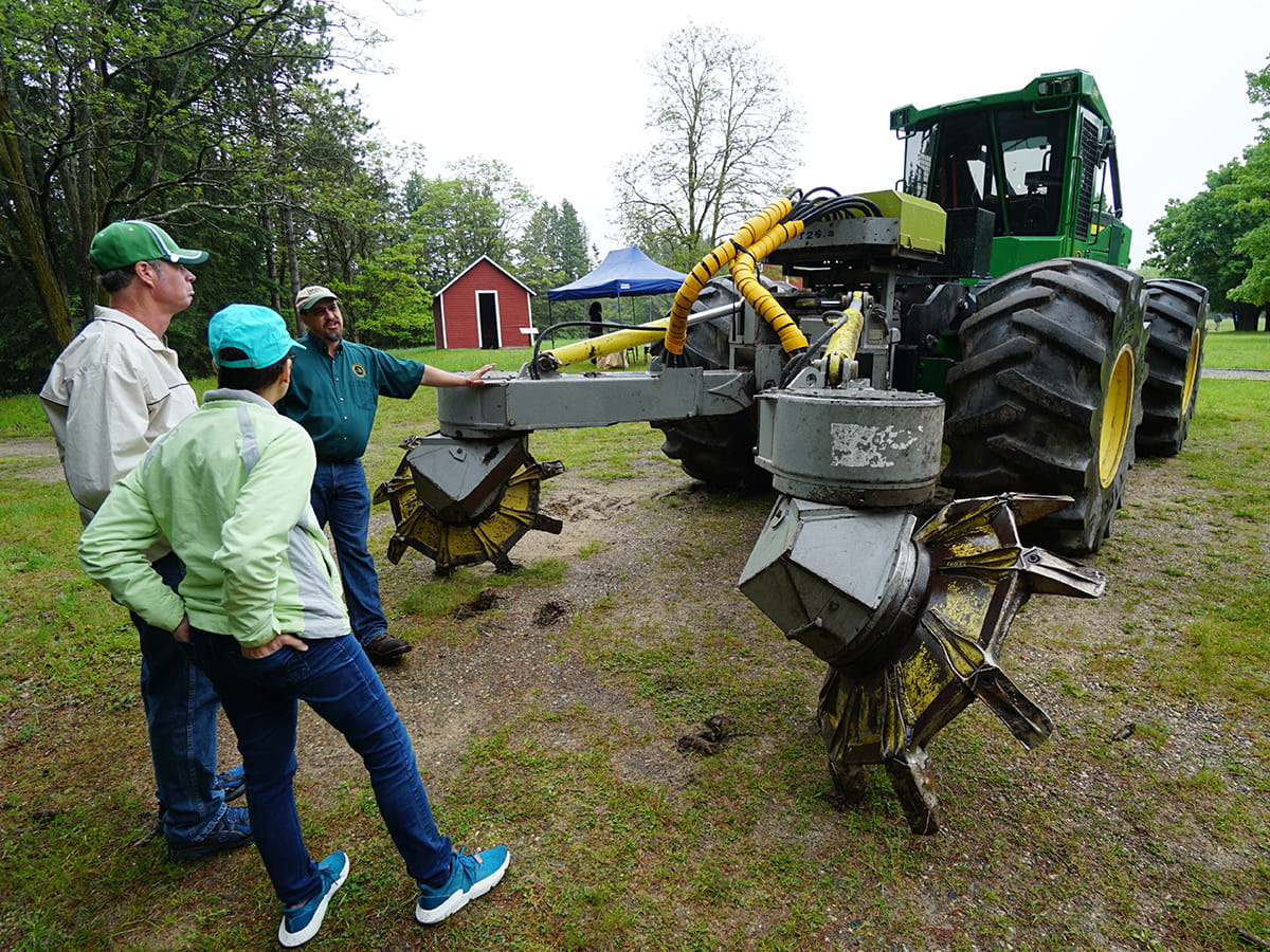 Three people standing and talking near forest service equipment at Higgins Lake Nursery.