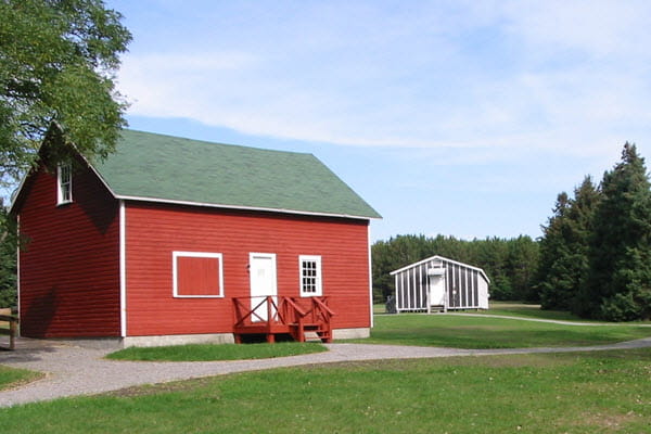 A gravel path winds its way from a red wooden work building to a baton and tar paper building in the background. 