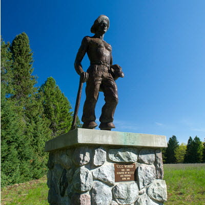 A bronze statue of a young man in a hat and with a shovel sits on a stone pillar.