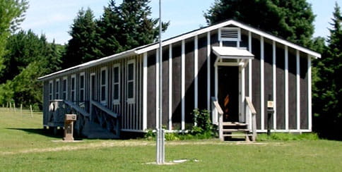 A long 1-story wooden building with baton and tar siding. 