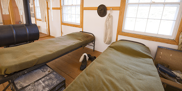 Reconstructed camp beds with green blankets on display.