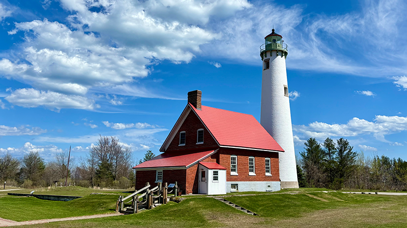 A lighthouse with a white tower and a red brick building attached.