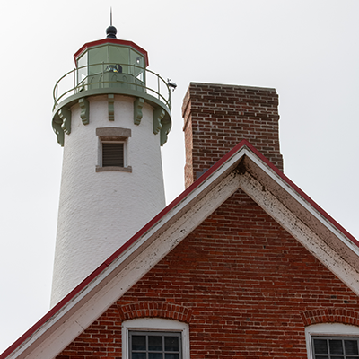 The top portion of a white tower lighthouse with a brick keeper's dwelling.