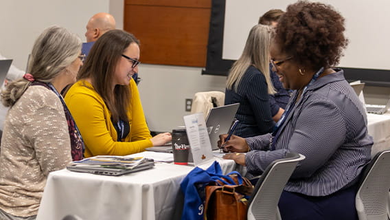 three people sit together at a table in a conference center