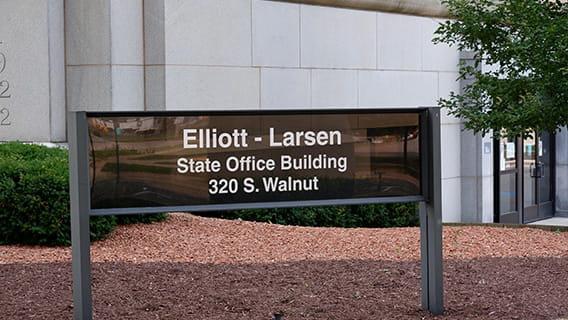 photo of a sign reading "Elliot-Larsen, State Office Building, 320 S. Walnut" in front of the Elliot-Larsen building in Lansing, Michigan