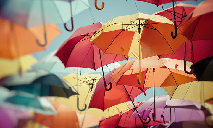 photo of multiple umbrellas of different colors floating against a flat blue grey background