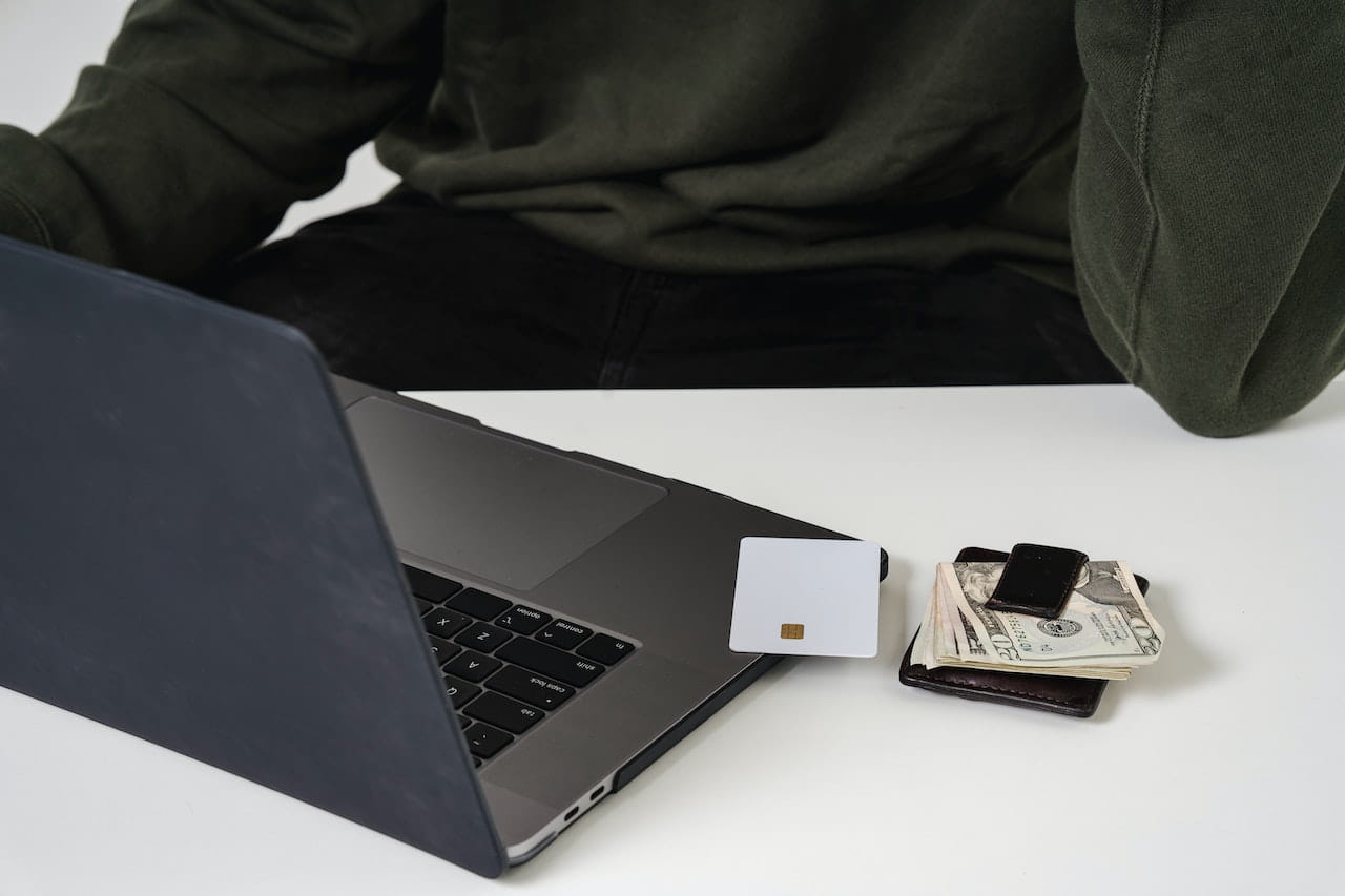 Open laptop on table next to credit card and money.