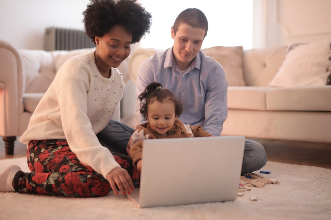 Parents and child sitting on floor on laptop.