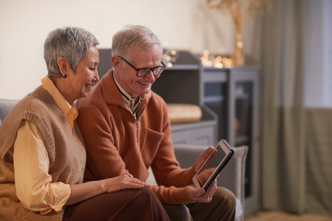 Two senior citizens looking at tablet while sitting on sofa.