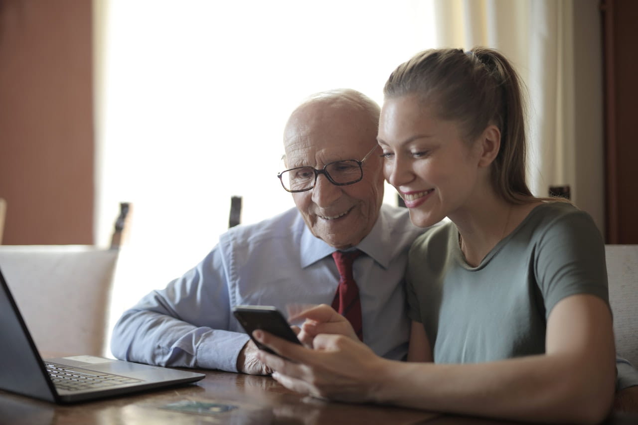 Elderly man and young woman on laptop while sitting at a table.