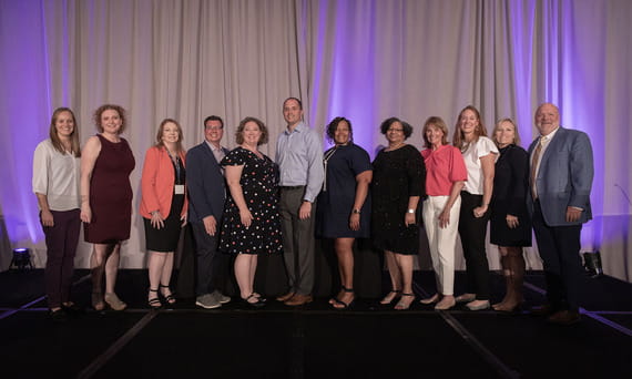 Michigan Office of Retirement Services (ORS) Plan Development and Compliance Director Allison Wardlaw, joined by three men and eight other women on stage, accepting recognition for ORS as PlanSponsor’s 2024 Plan Sponsor of the Year award in Chicago.