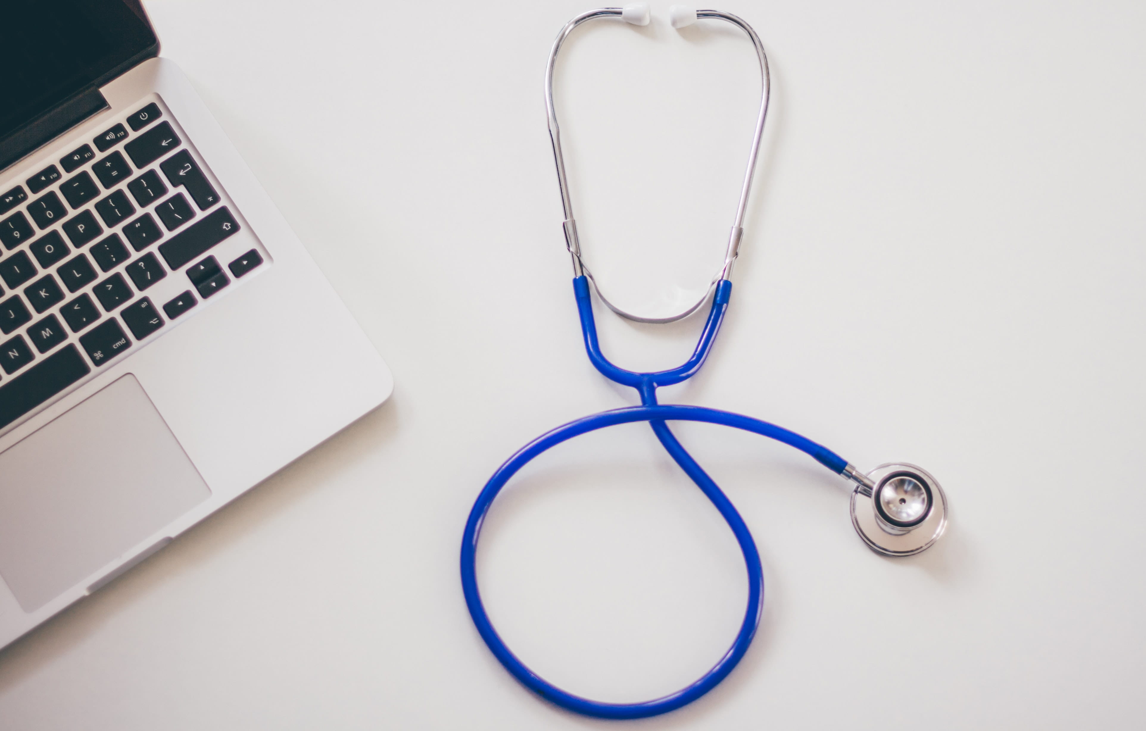 A blue stethoscope laying on a desk next to a laptop