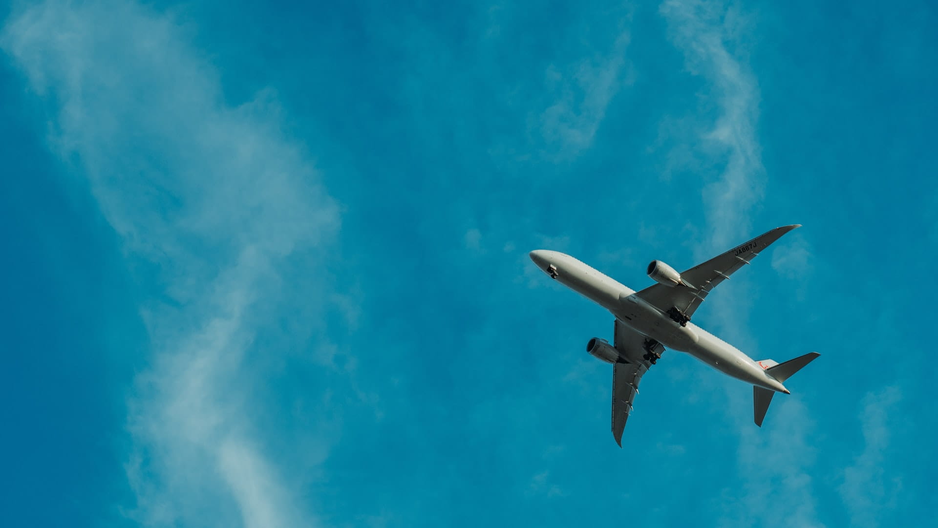 An airplane in the air with a bright blue lightly cloudy sky behind it