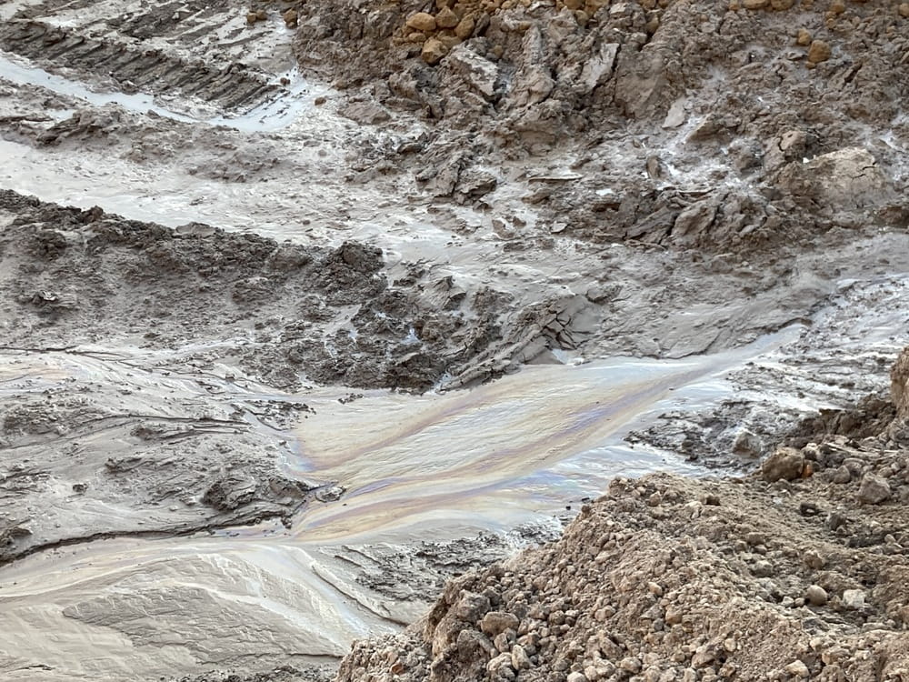 An oil sheen in a pile of mud, from a contamination site