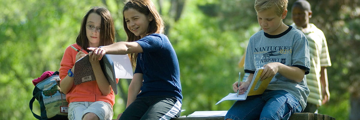 Kids sitting on a bench writing and pointing at things