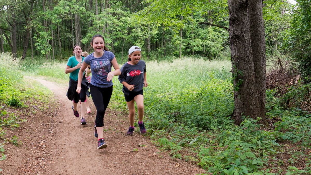 a group of children run down a trail in the forest